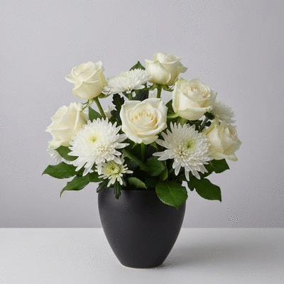 Composition florale sobre et élégante pour un deuil, avec des roses blanches et des chrysanthèmes, dans un vase discret